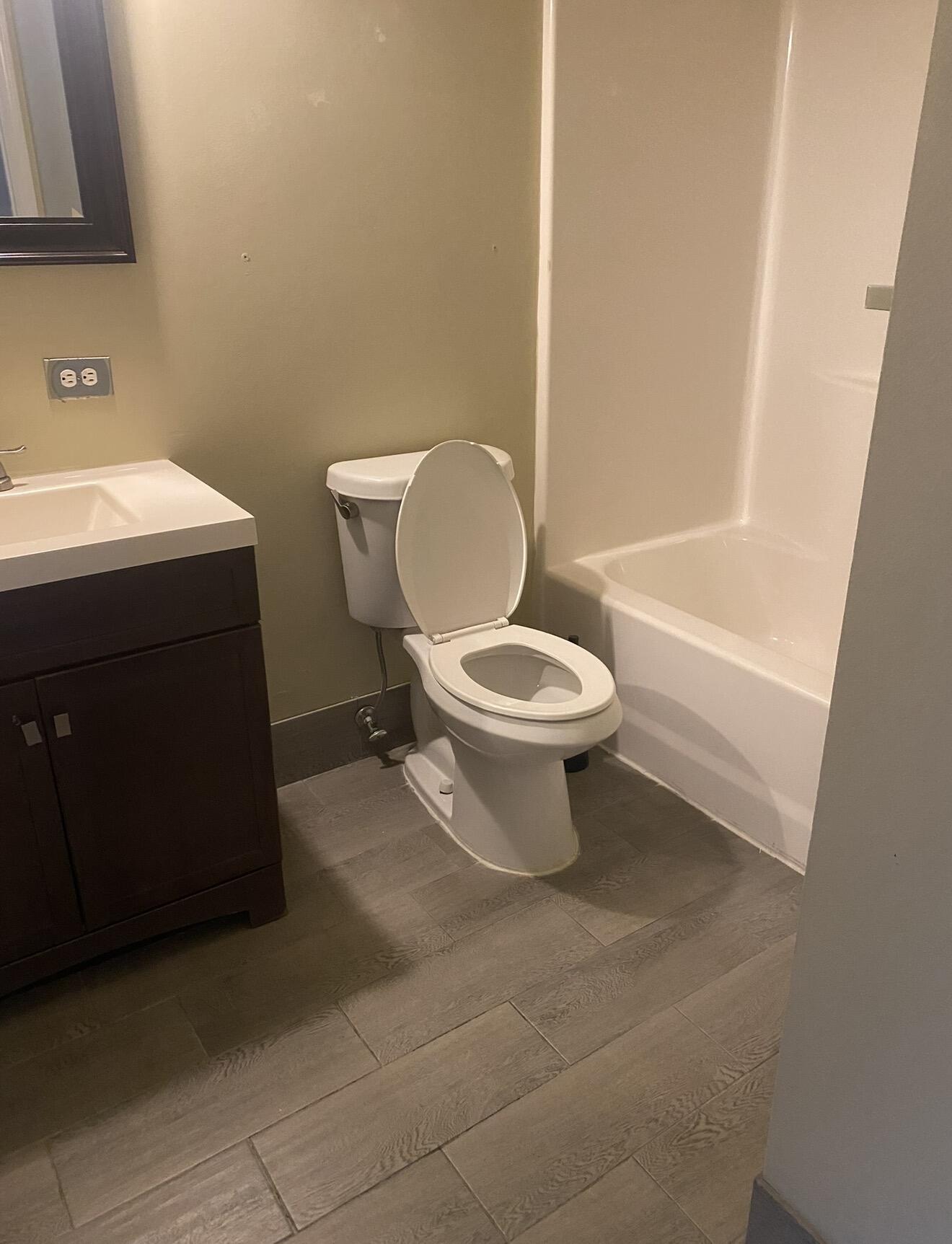 Bathroom with a dark wood vanity, white toilet, bathtub, and large wood-look floor tiles.