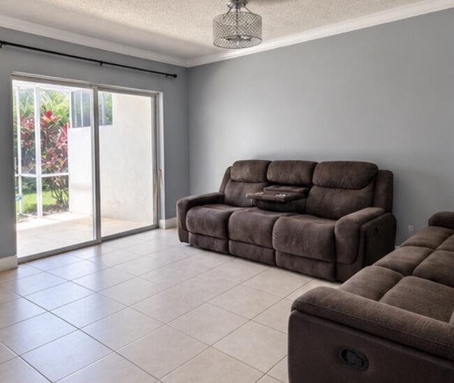 Living room with brown reclining sofas, tiled floors, and sliding glass doors opening to a garden.