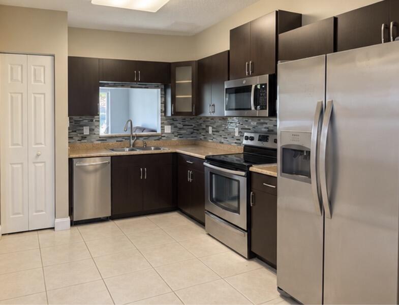 Kitchen with dark cabinets, stainless steel appliances, granite counters, and a mosaic tile backsplash.