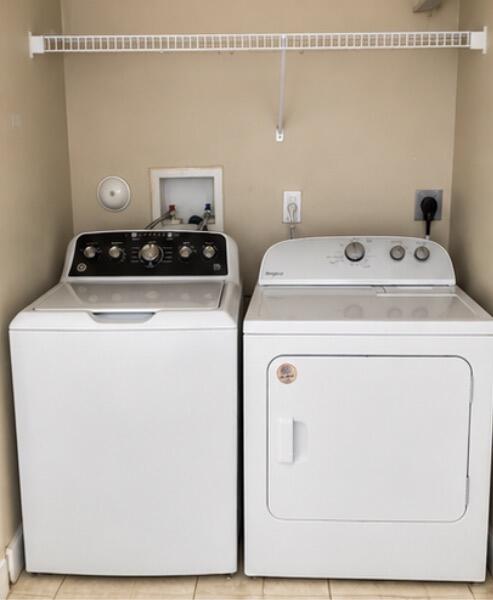 Laundry area with a top-loading washer and front-loading dryer beneath a wire shelf.