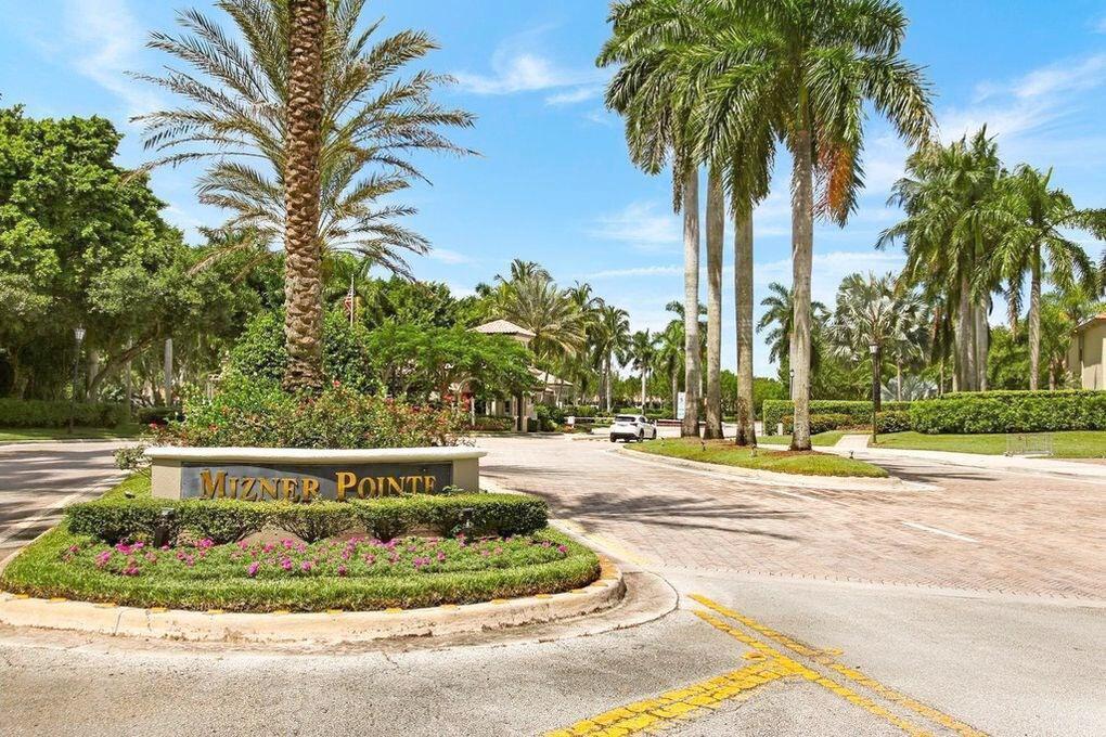 Mizner Pointe entrance sign surrounded by palm trees and flowering landscaping.