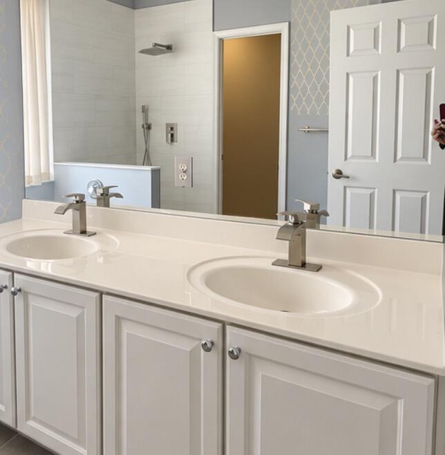 Bathroom with a white double-sink vanity and wide mirror reflecting a tiled shower.