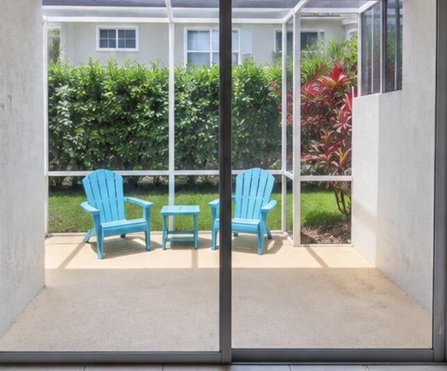 Screened patio with two turquoise chairs and a small table overlooking a hedge and tropical plants.