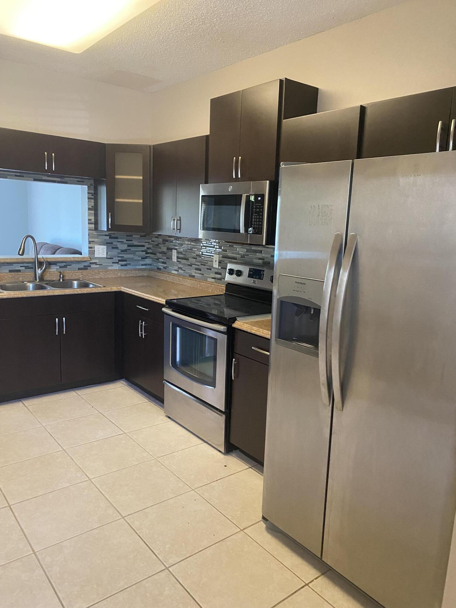 Kitchen with dark cabinets, stainless steel appliances, and a gray mosaic backsplash.