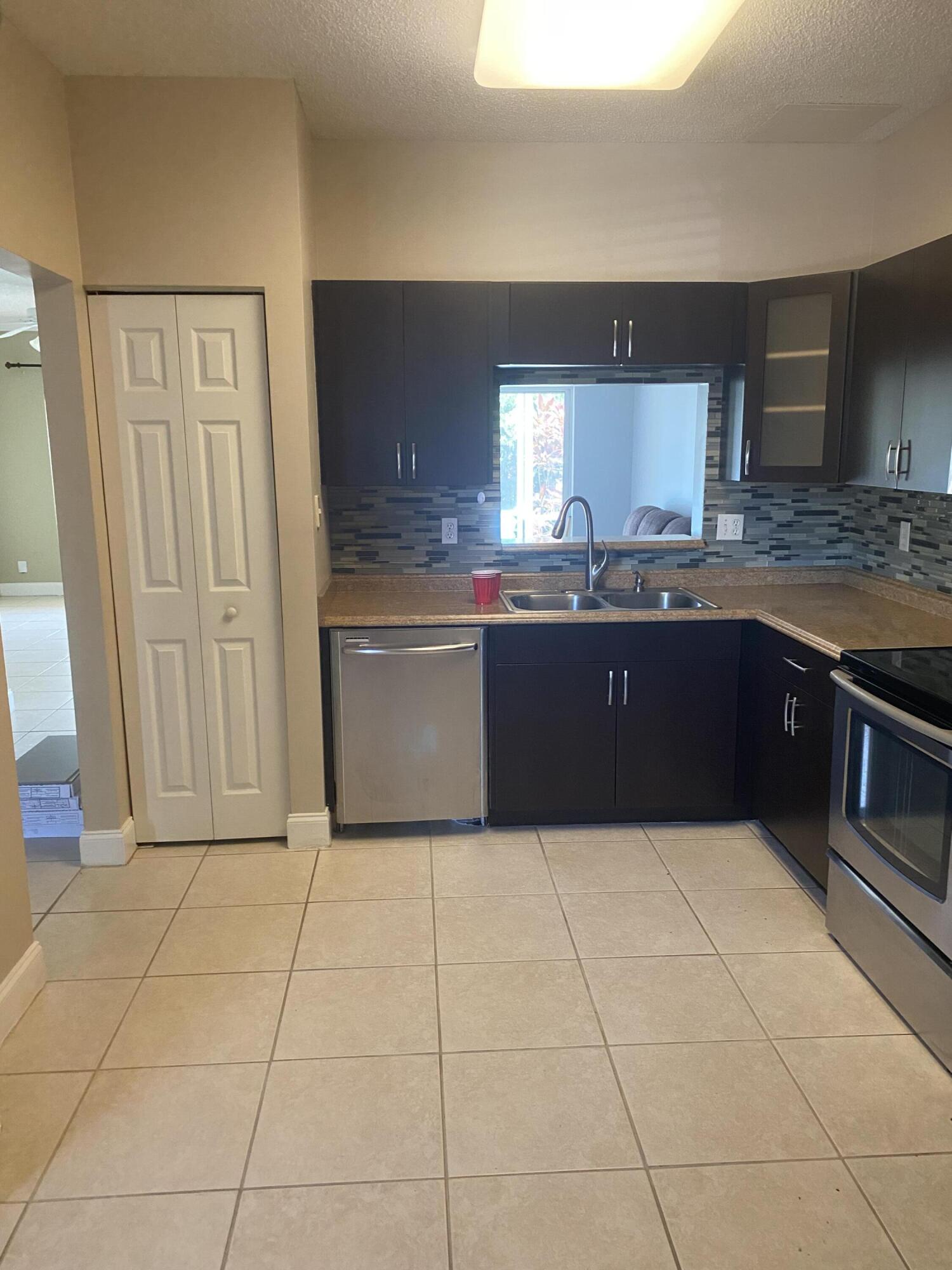 Kitchen with dark cabinets, stainless steel appliances, and a double-basin sink beneath a pass-through window.