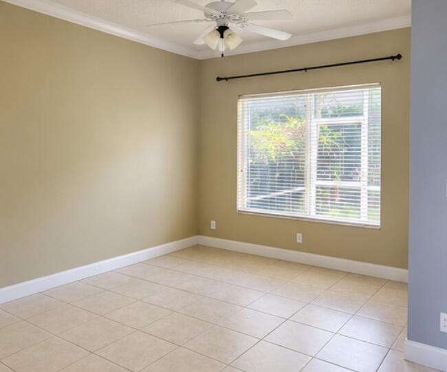 Empty beige room with tiled floors, a ceiling fan, and a wide window with white blinds.