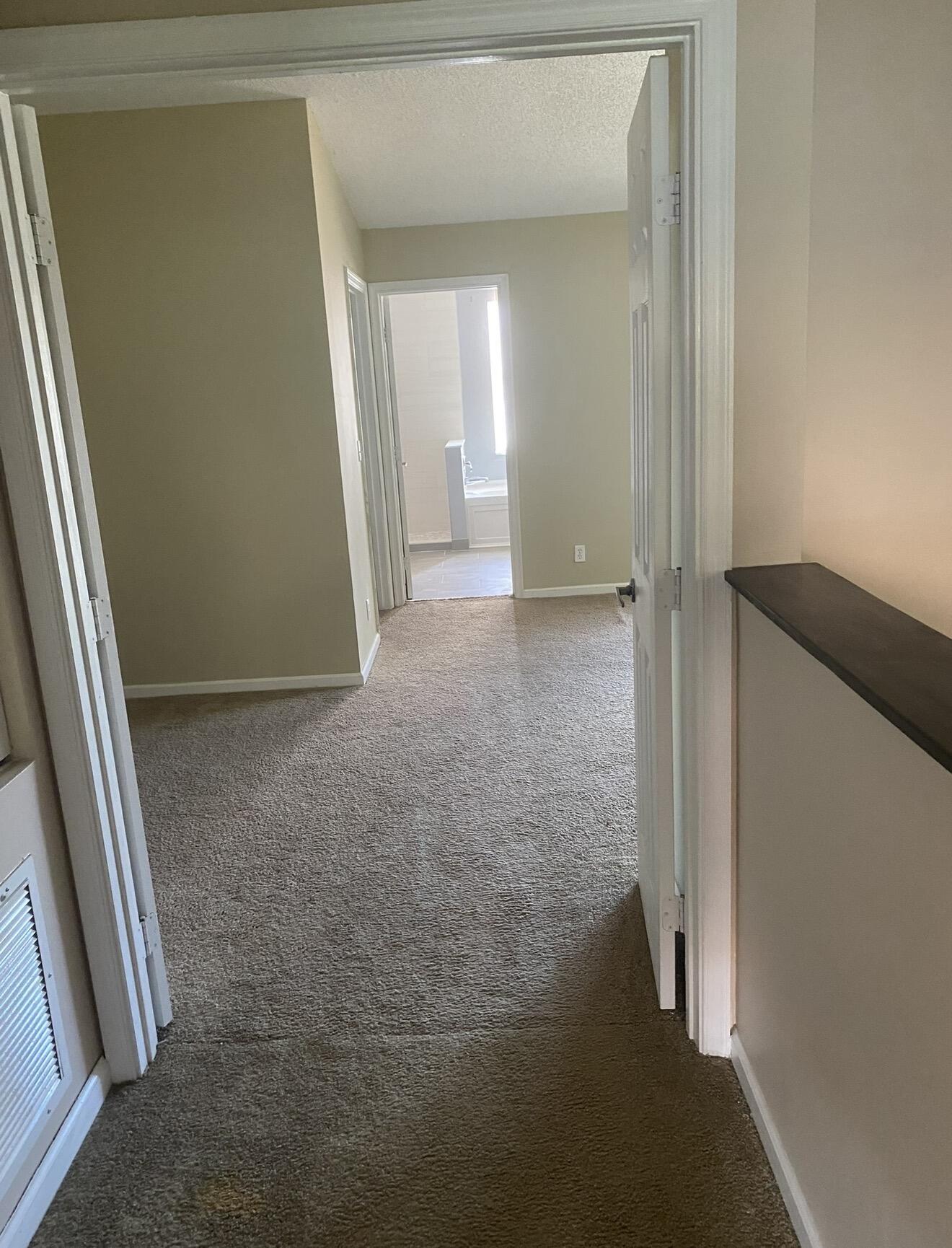 Carpeted hallway with open doorways leading to a bright bathroom.