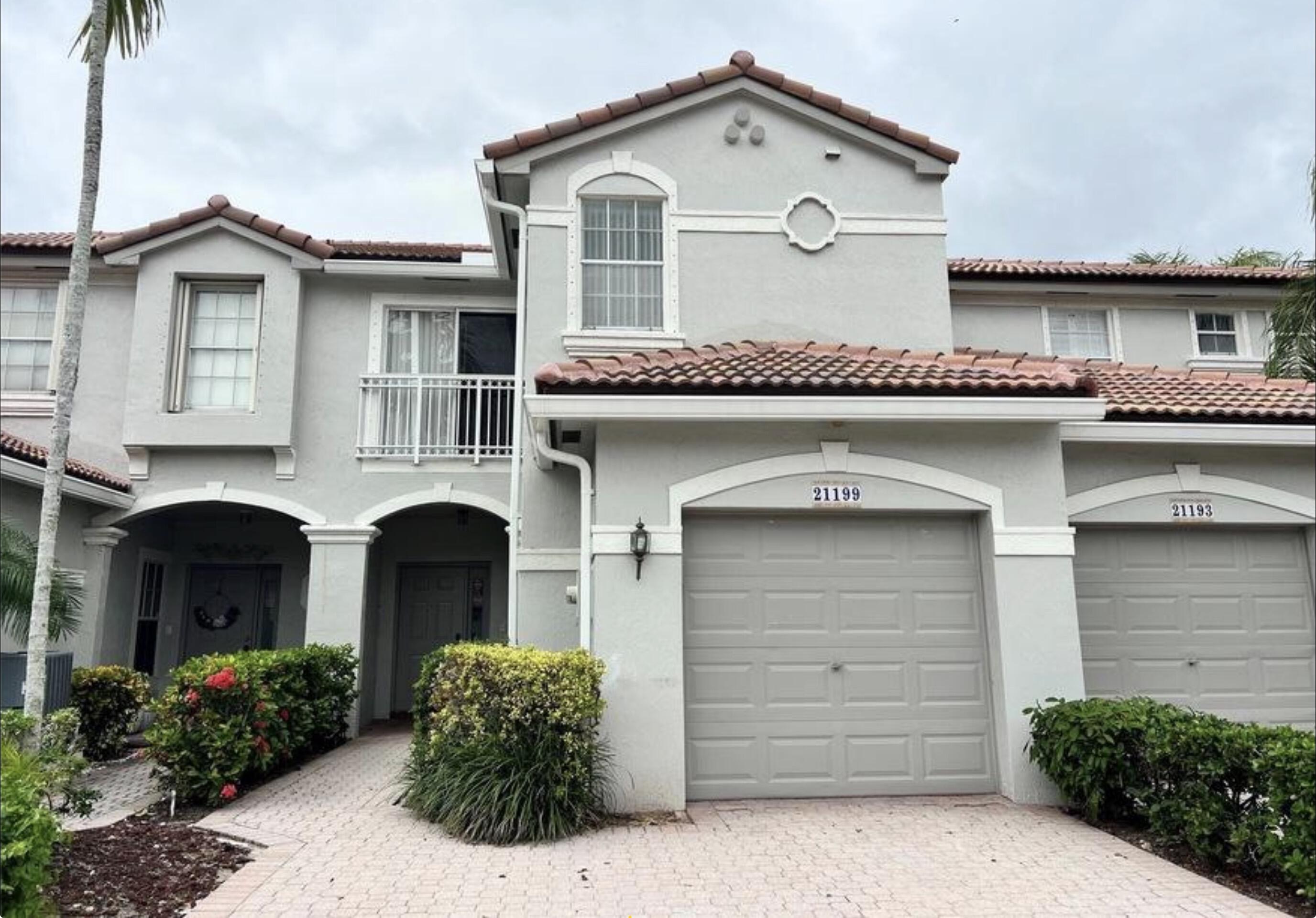 Two-story stucco townhouse with terracotta tile roofs, attached garages, and a landscaped covered entry.