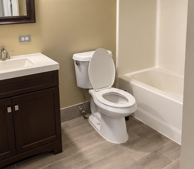 Bathroom with a dark wood vanity, white toilet, bathtub, and beige tile floor.