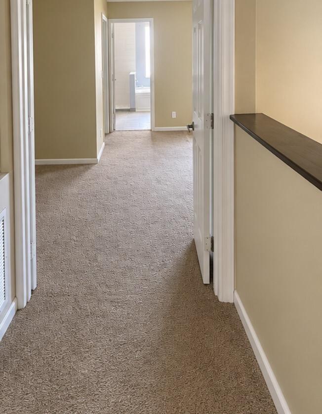 Empty carpeted hallway with beige walls, multiple doorways, and a dark ledge along the right wall.