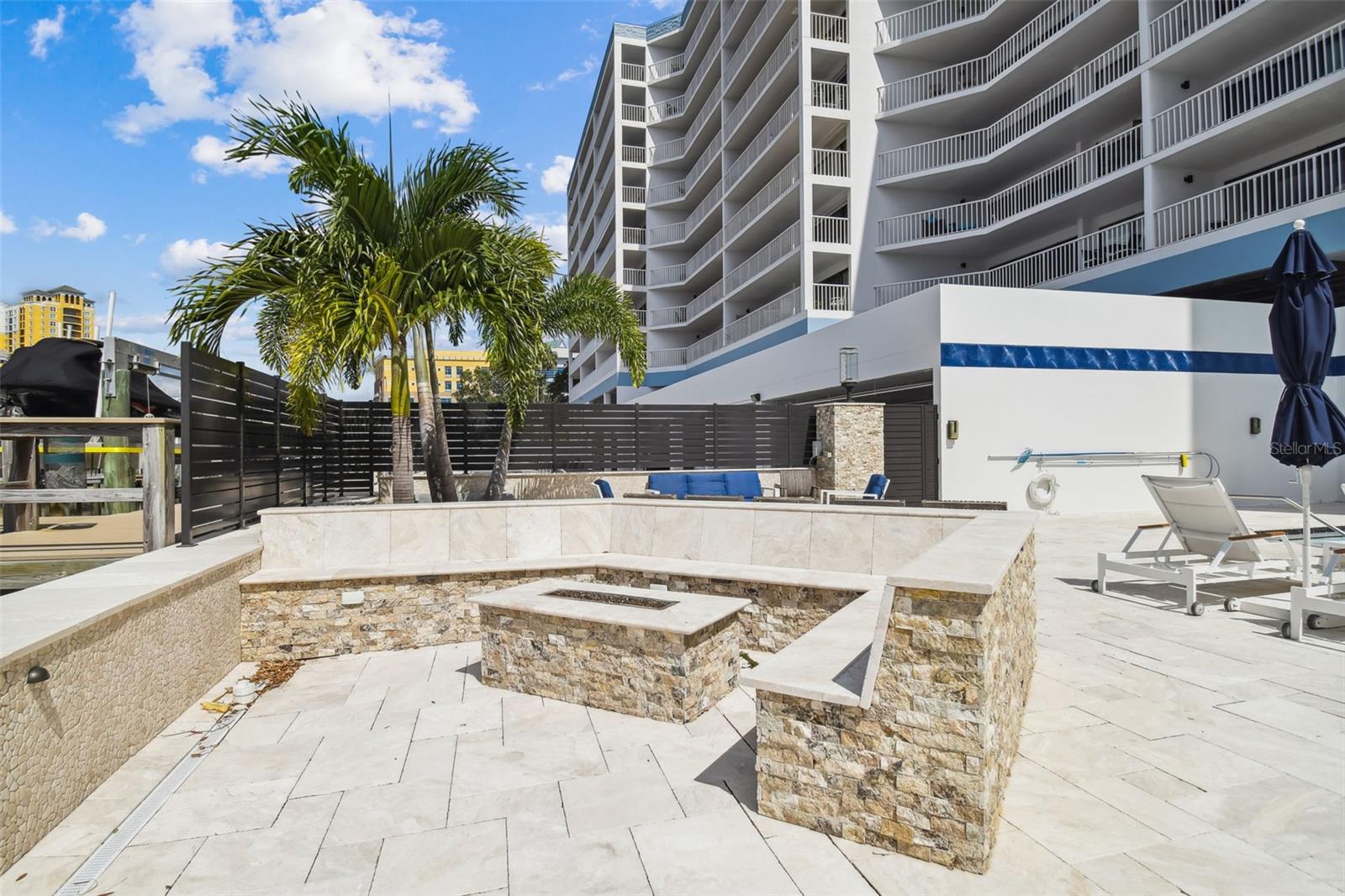 Condominium courtyard with stone fire pit seating, palm trees, and lounge chairs.