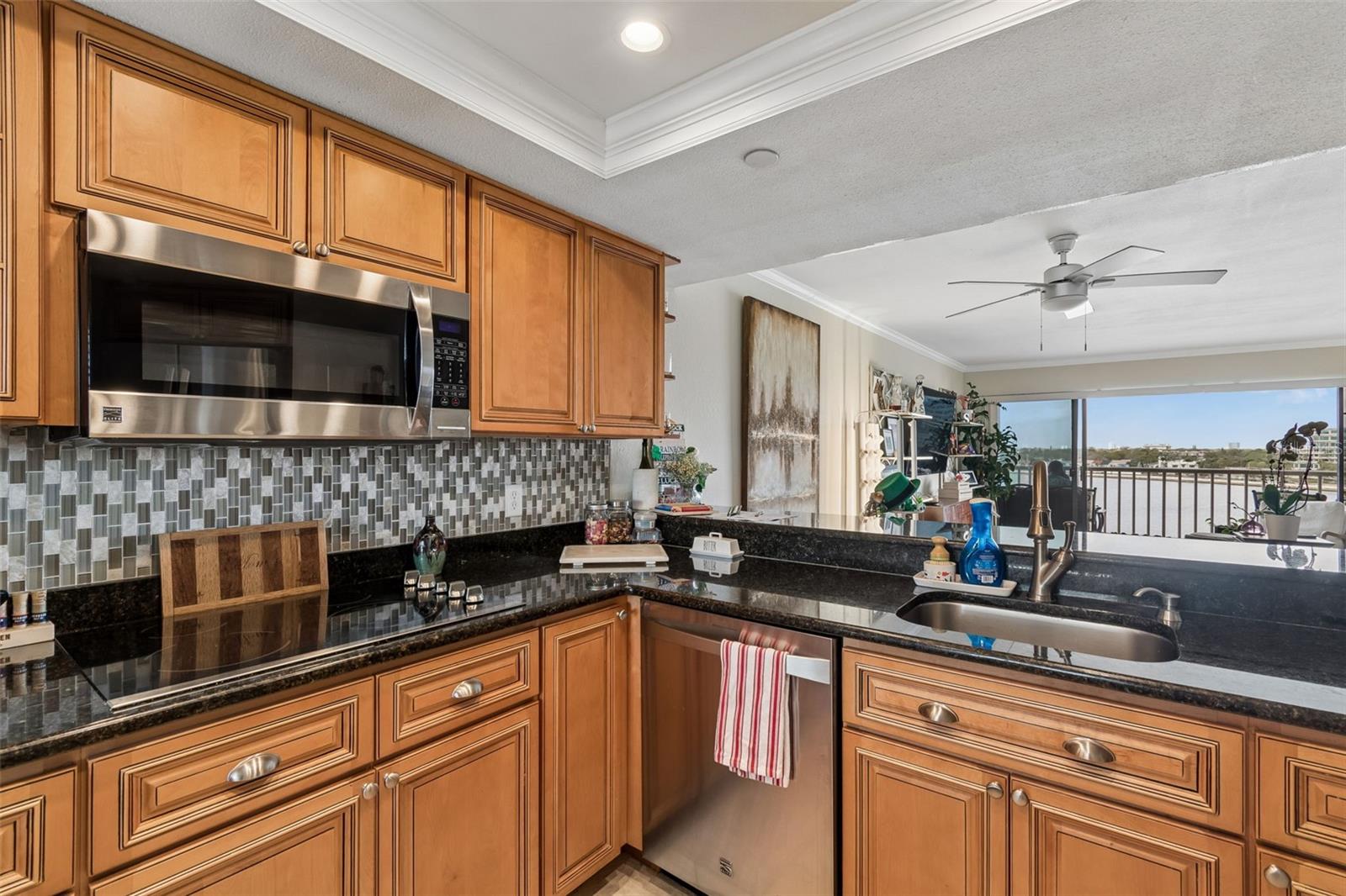 Condo kitchen with honey-colored cabinets, black granite counters, and a balcony view of the water.