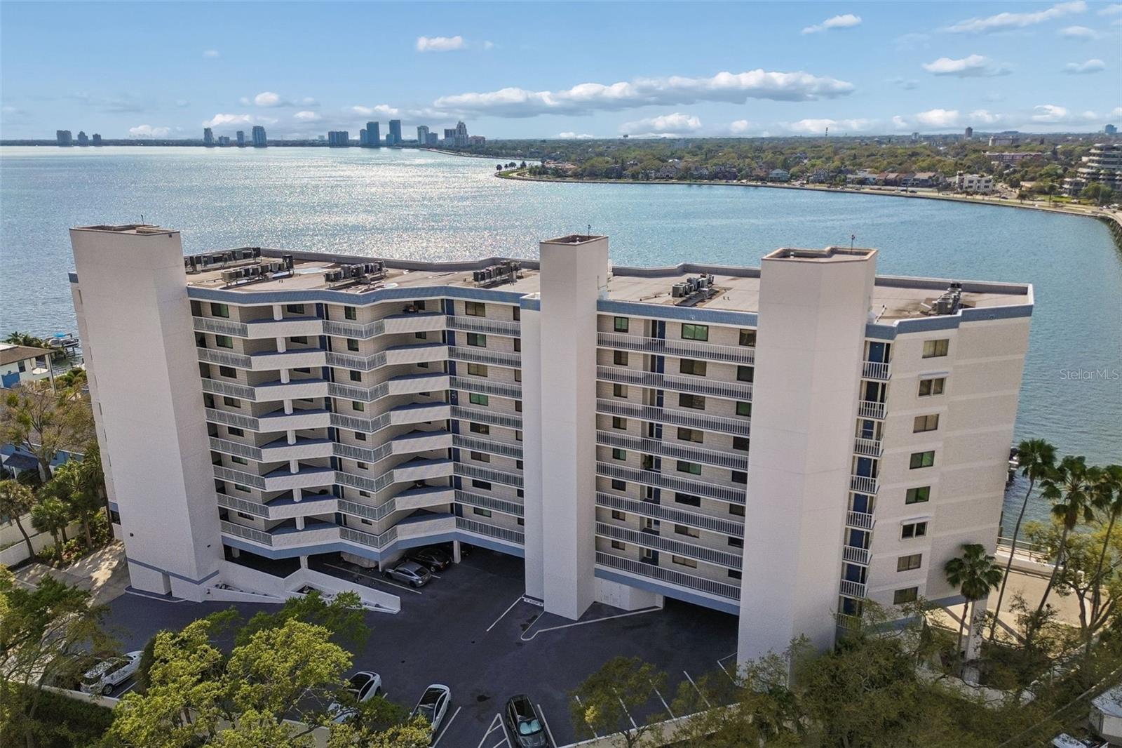 Waterfront condominium building with stacked balconies, Tampa Bay, and a distant city skyline.