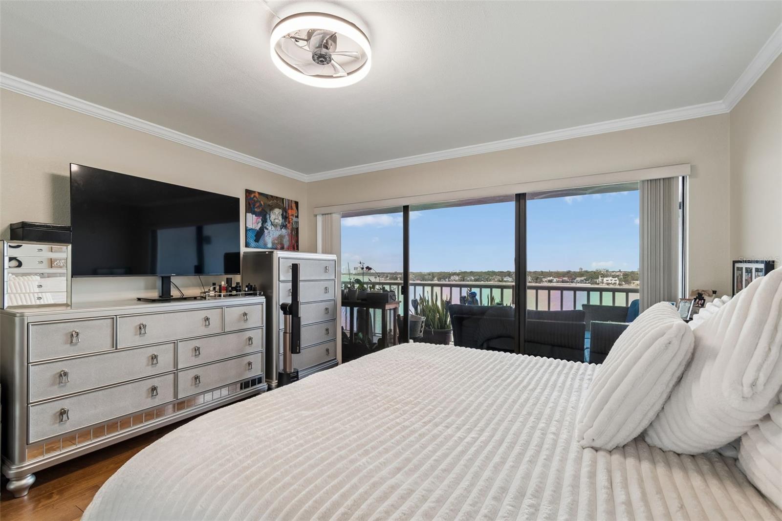 Furnished bedroom with a large white bed and sliding glass doors overlooking the water.