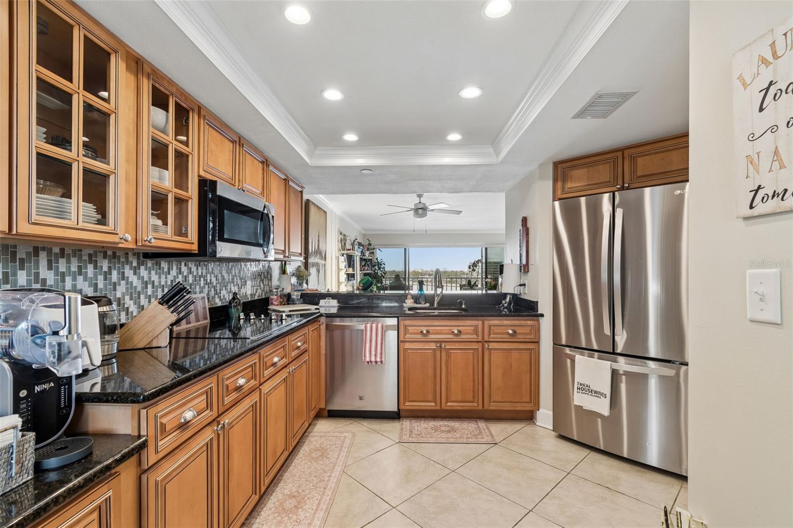 Kitchen with warm wood cabinetry, black granite counters, stainless appliances, and a window overlooking the surrounding area.
