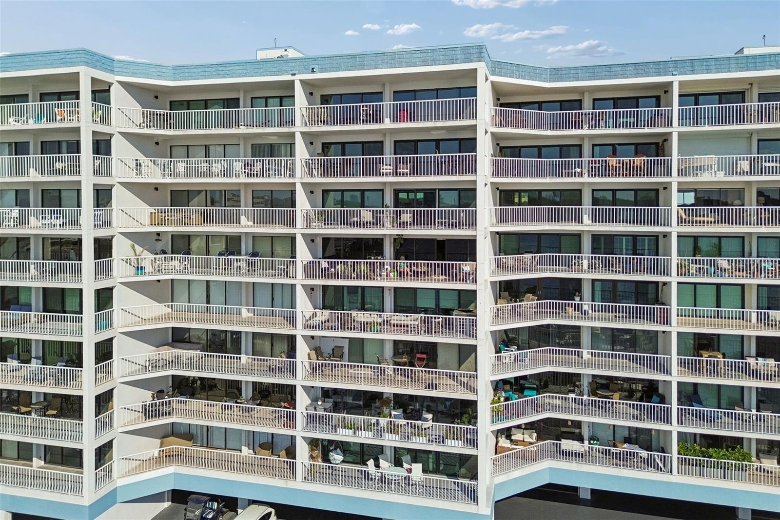 Condominium building with rows of white-railed balconies, patio furniture, and blue roof trim.