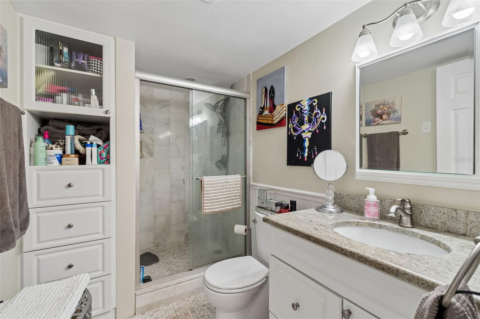 Bathroom with a glass-enclosed marble shower, granite vanity countertop, and built-in white storage.