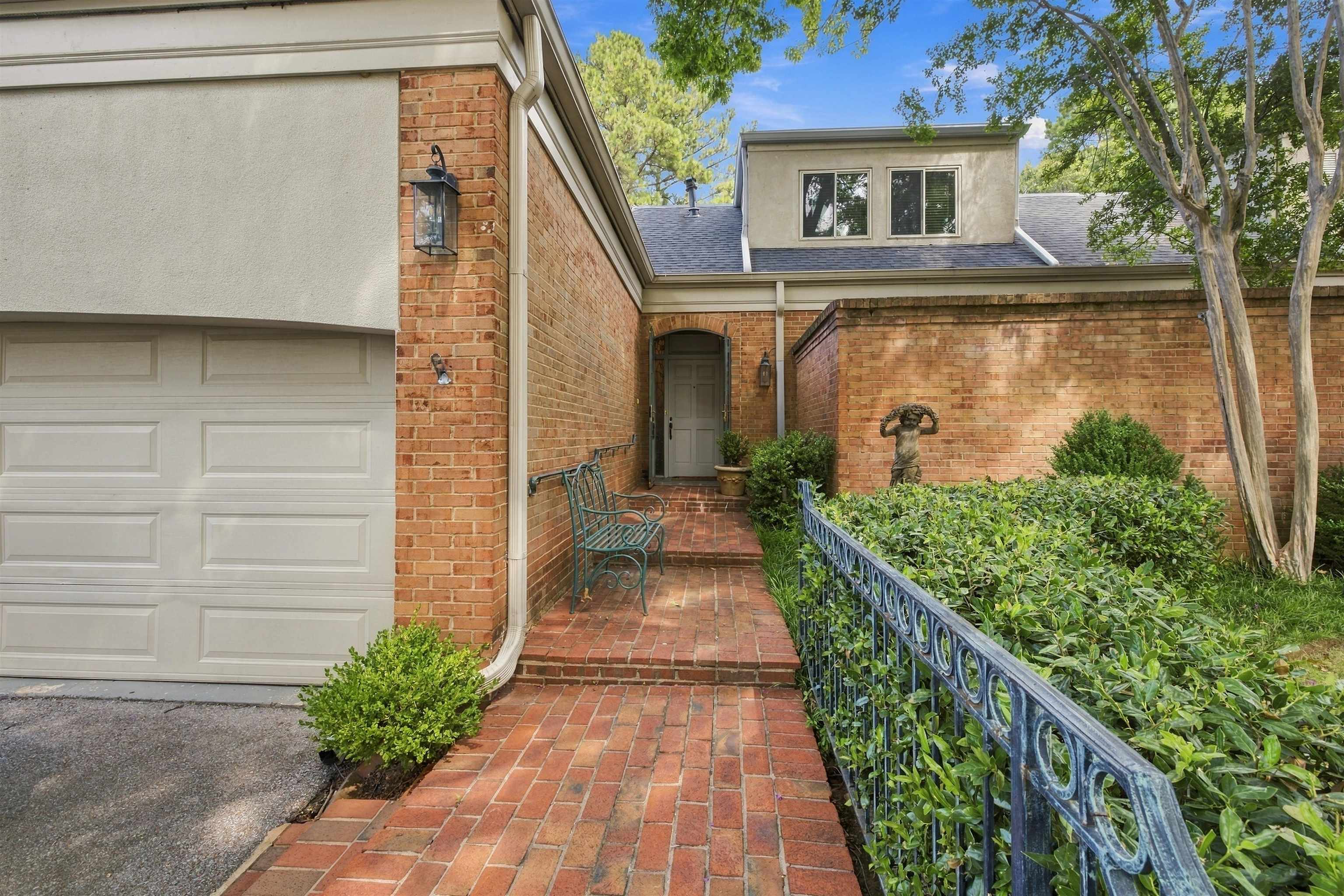 Brick home entrance with a red brick walkway, iron railing, and garden statue.