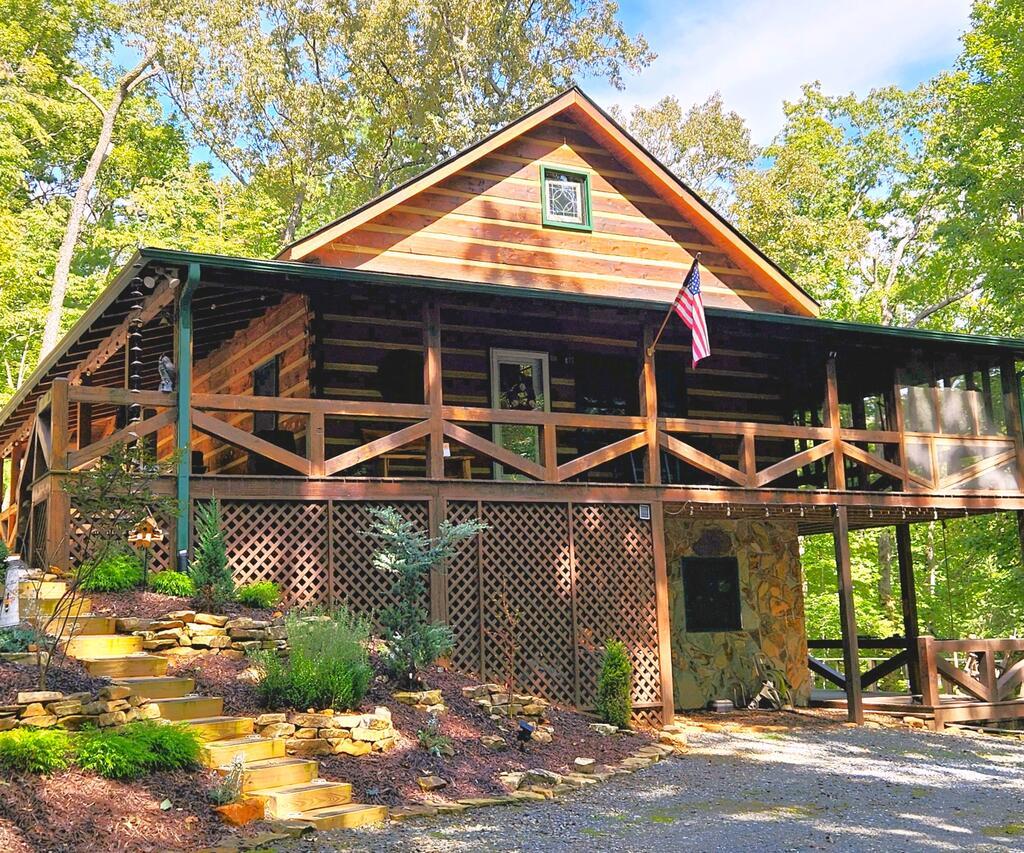 Wood cabin with a covered porch and stone foundation, surrounded by trees and landscaped steps.