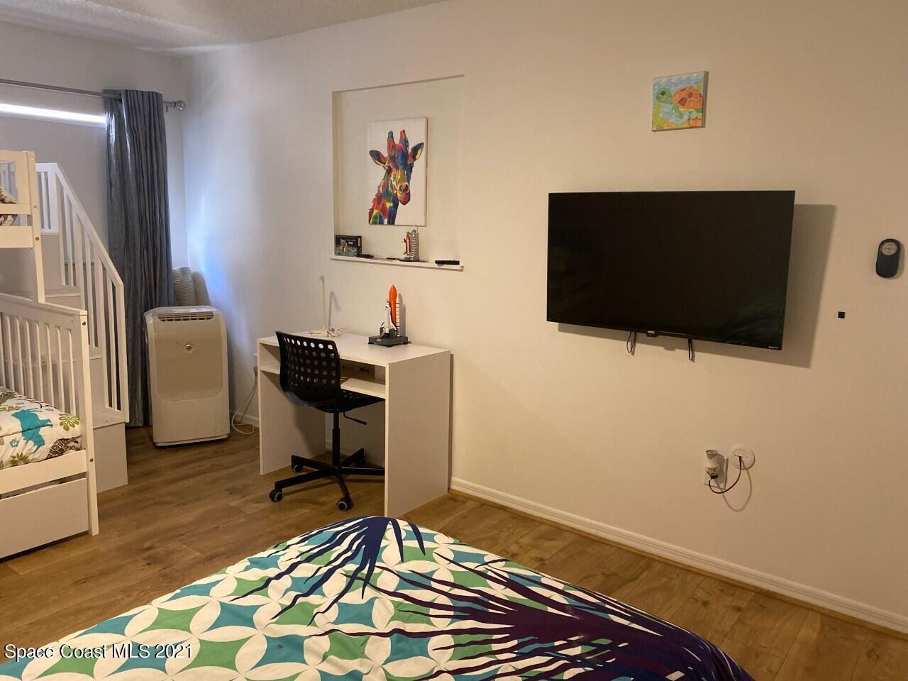 Bedroom with a desk and wall-mounted television beside a white bunk bed.
