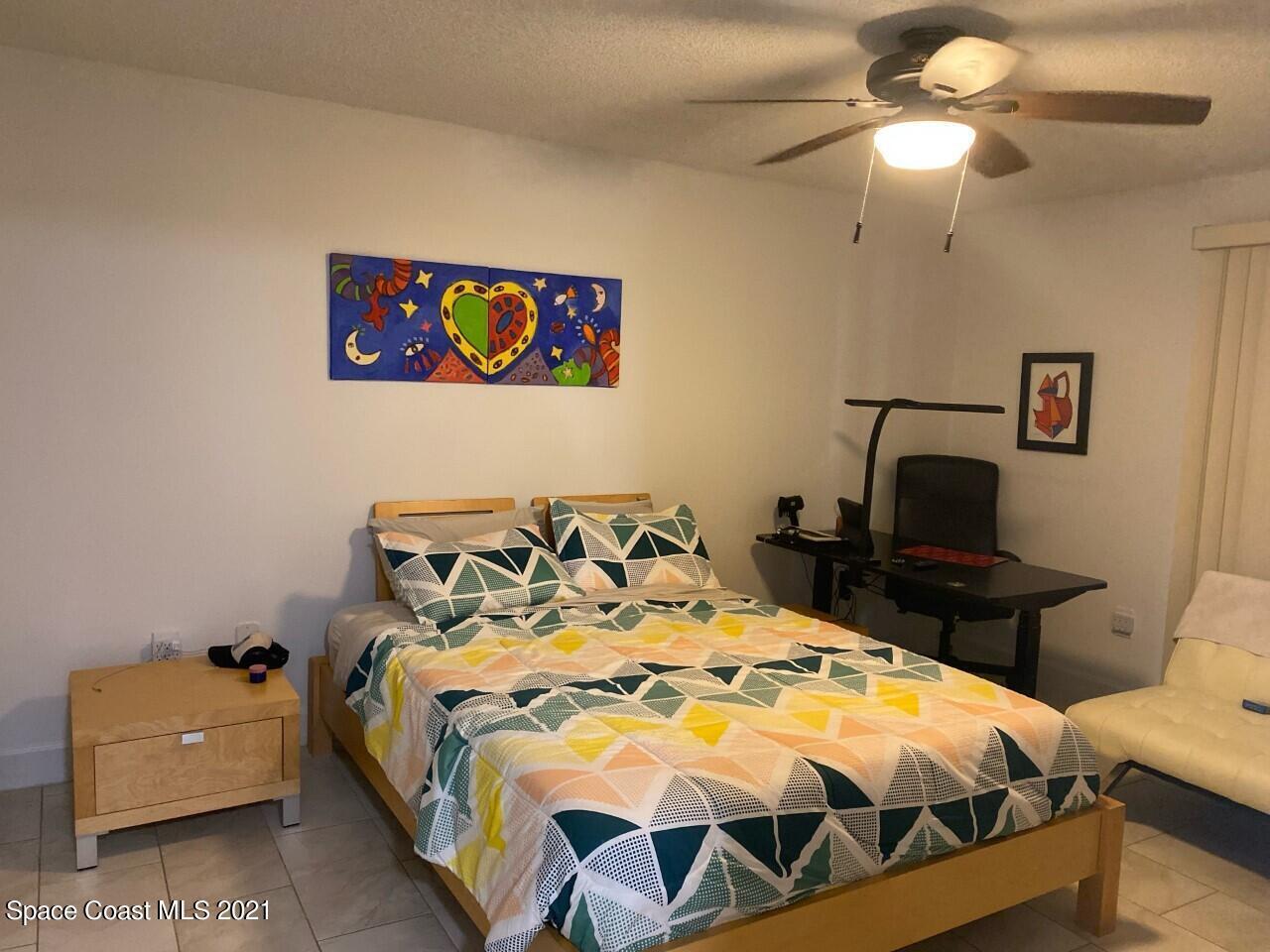 Bedroom with colorful geometric bedding, a ceiling fan, and a desk and chair.