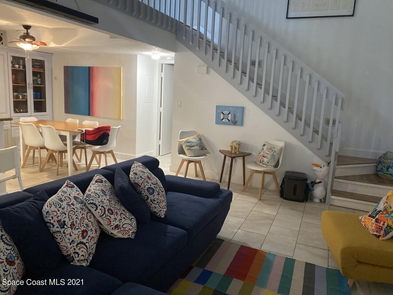 Living and dining room with a navy sectional, colorful rug, and prominent staircase.