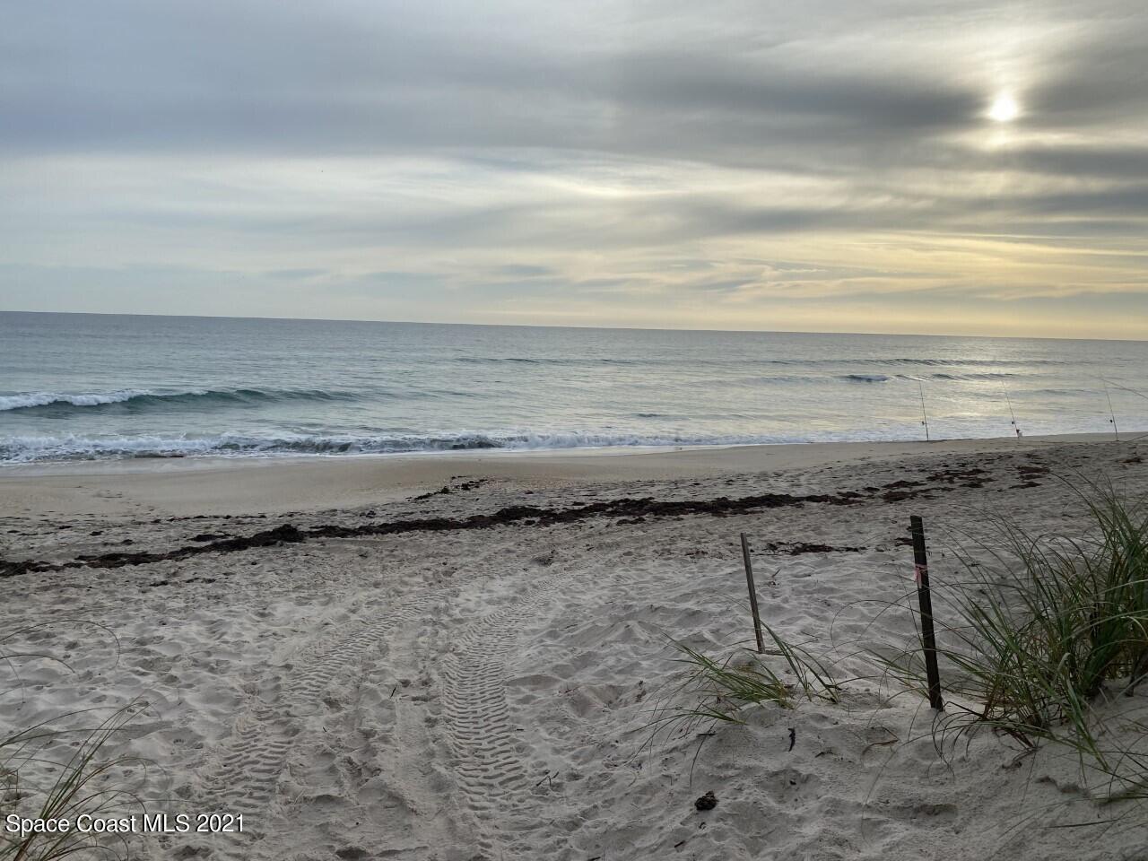 Sandy beach and ocean with fishing rods, sea oats, and a low sun behind clouds.