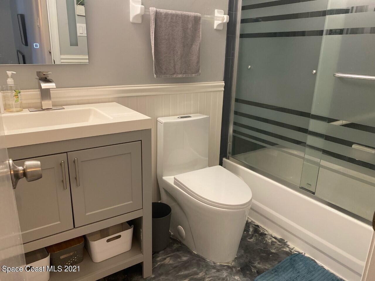 Bathroom with gray vanity, white toilet, and bathtub behind a striped glass shower screen.