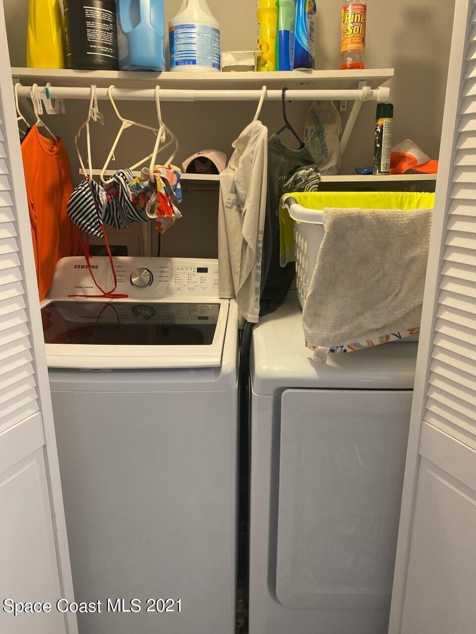 Laundry closet with a top-loading washer and dryer beneath shelves of cleaning supplies.