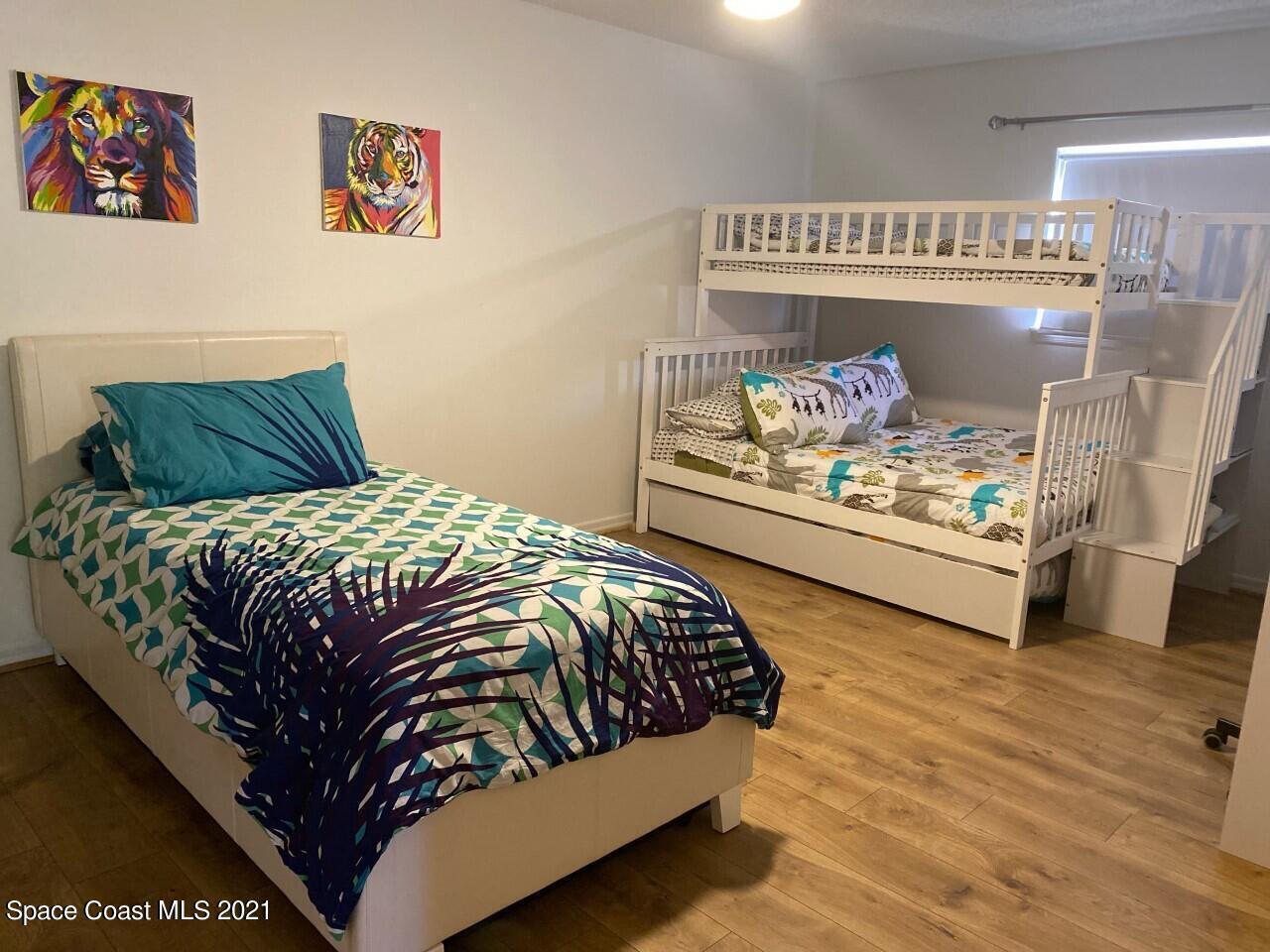 Bedroom with a double bed and white bunk bed, colorful bedding, and tiger artwork.