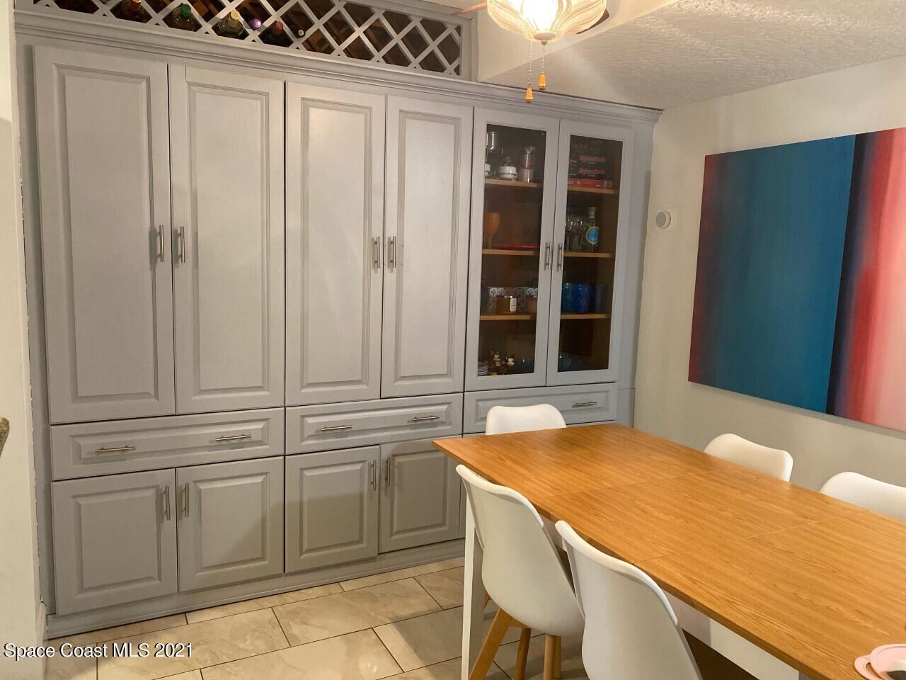Dining room with gray built-in cabinets, glass-front shelves, and a wooden table with white chairs.