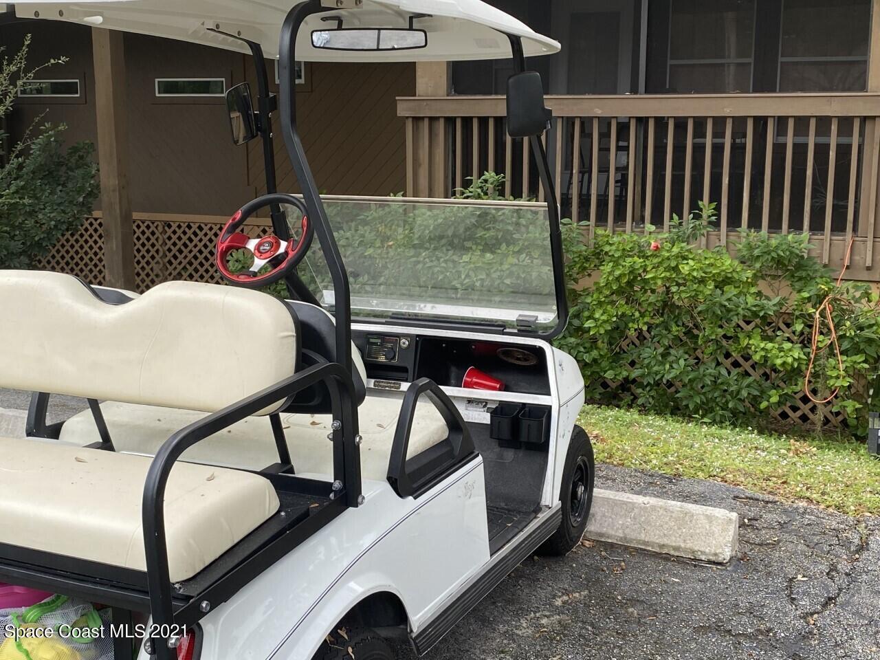 White golf cart parked beside a wooden home’s raised porch and shrubs.