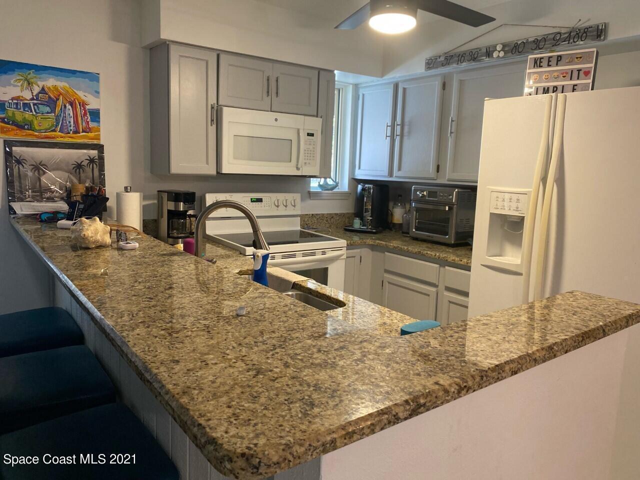 Kitchen with white cabinets and appliances, granite countertops, and a large breakfast bar with an inset sink.