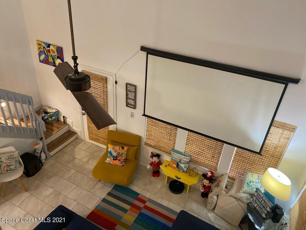 Living room with a large projection screen, ceiling fan, mustard-yellow chaise, and staircase.