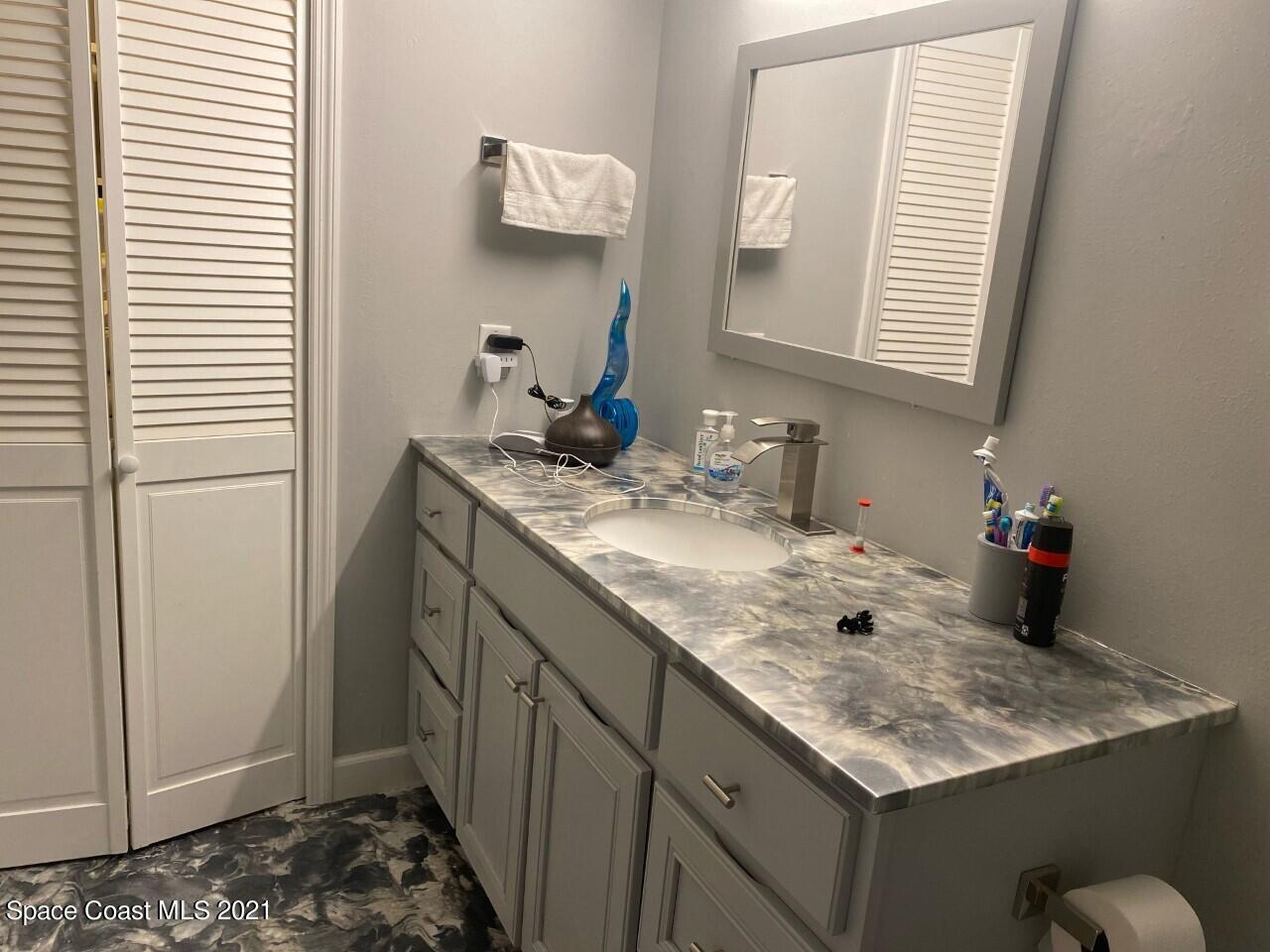 Bathroom vanity with gray cabinets, a marbled countertop, single sink, and large framed mirror.
