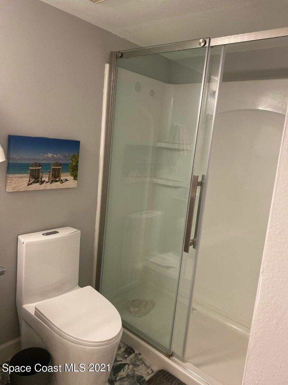 Bathroom with a glass-enclosed shower, built-in shelves, and a white toilet.