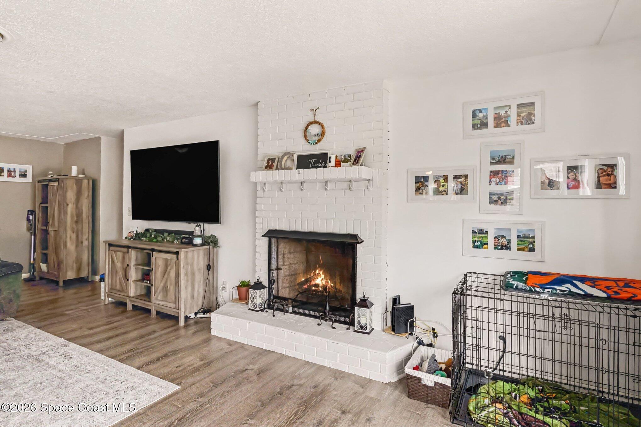 Living room with a lit brick fireplace, wall-mounted TV, and large dog crate.