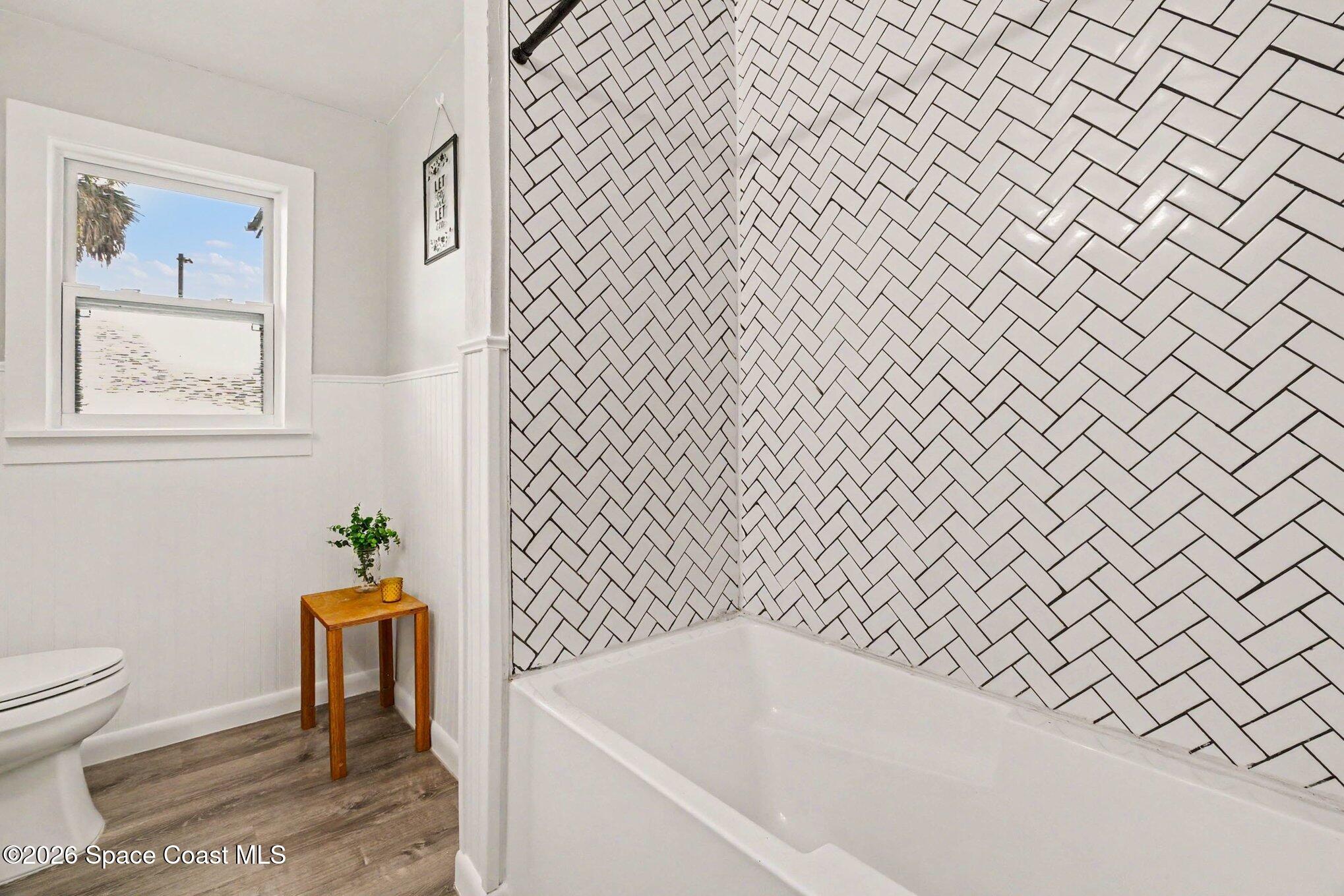 Bathroom with a white tub, bold herringbone tile surround, and a window beside the toilet.