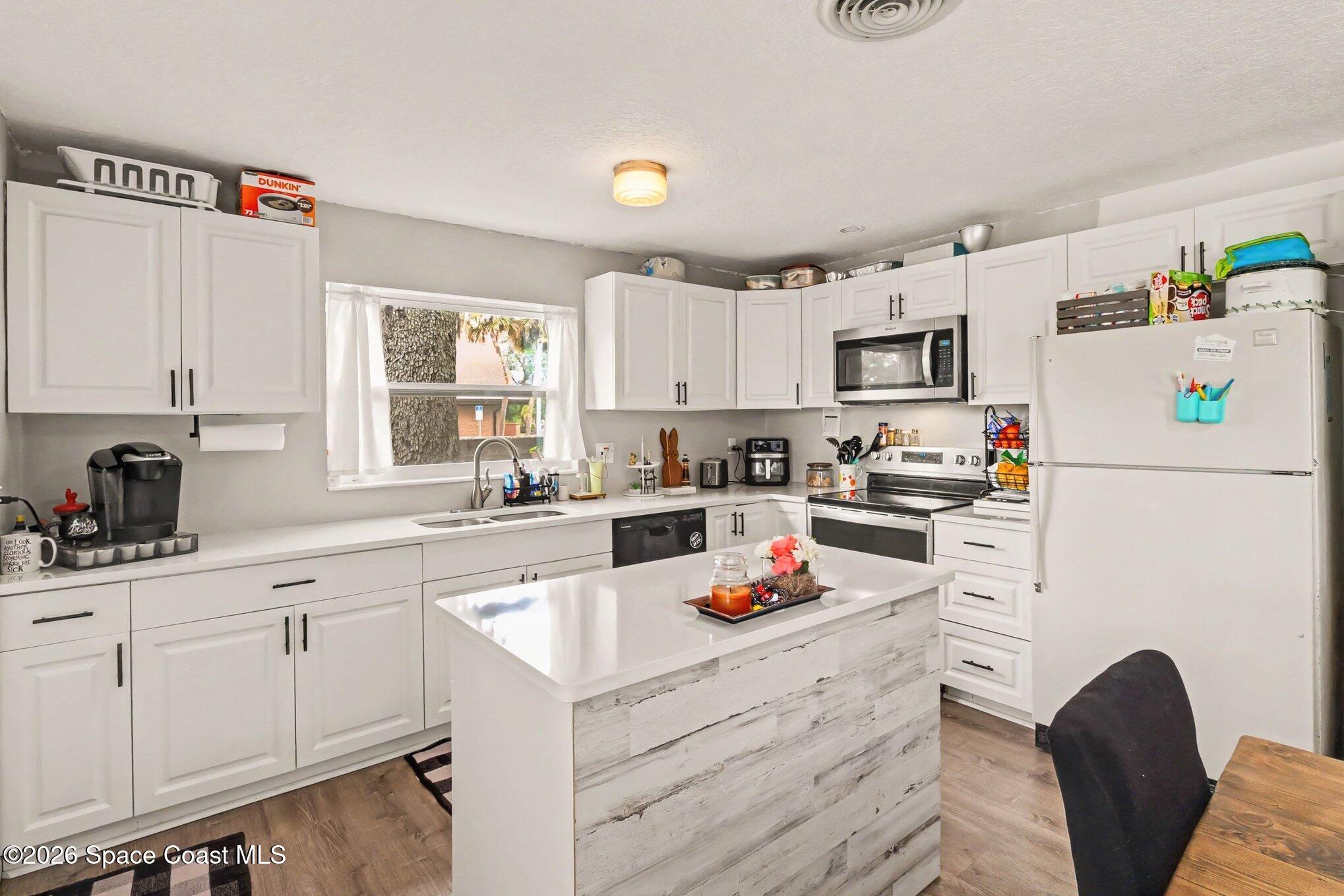 Kitchen with white cabinets, stainless appliances, and a large island with a weathered wood front.
