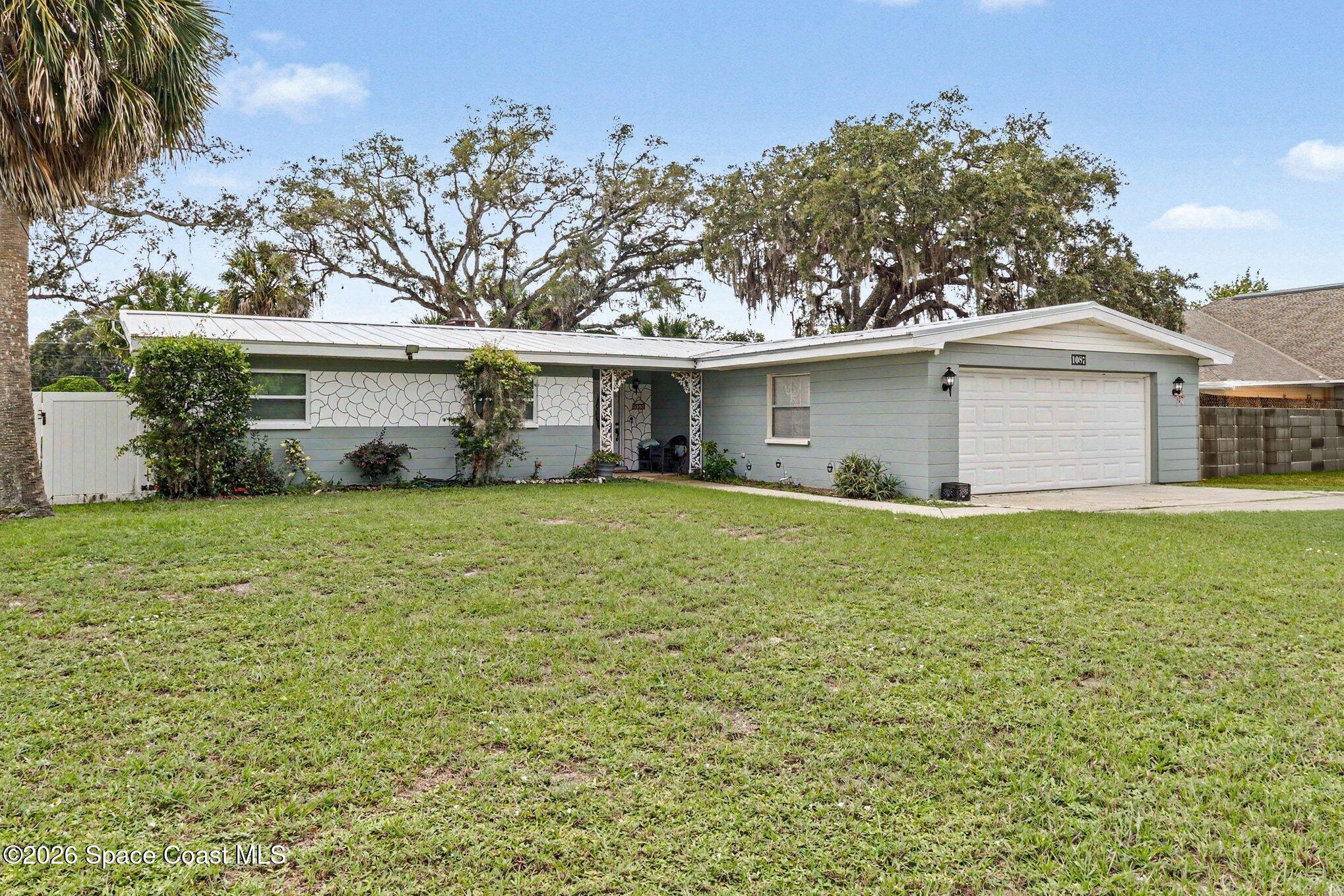 Single-story gray home with a white garage, decorative stone facade, and broad front lawn.