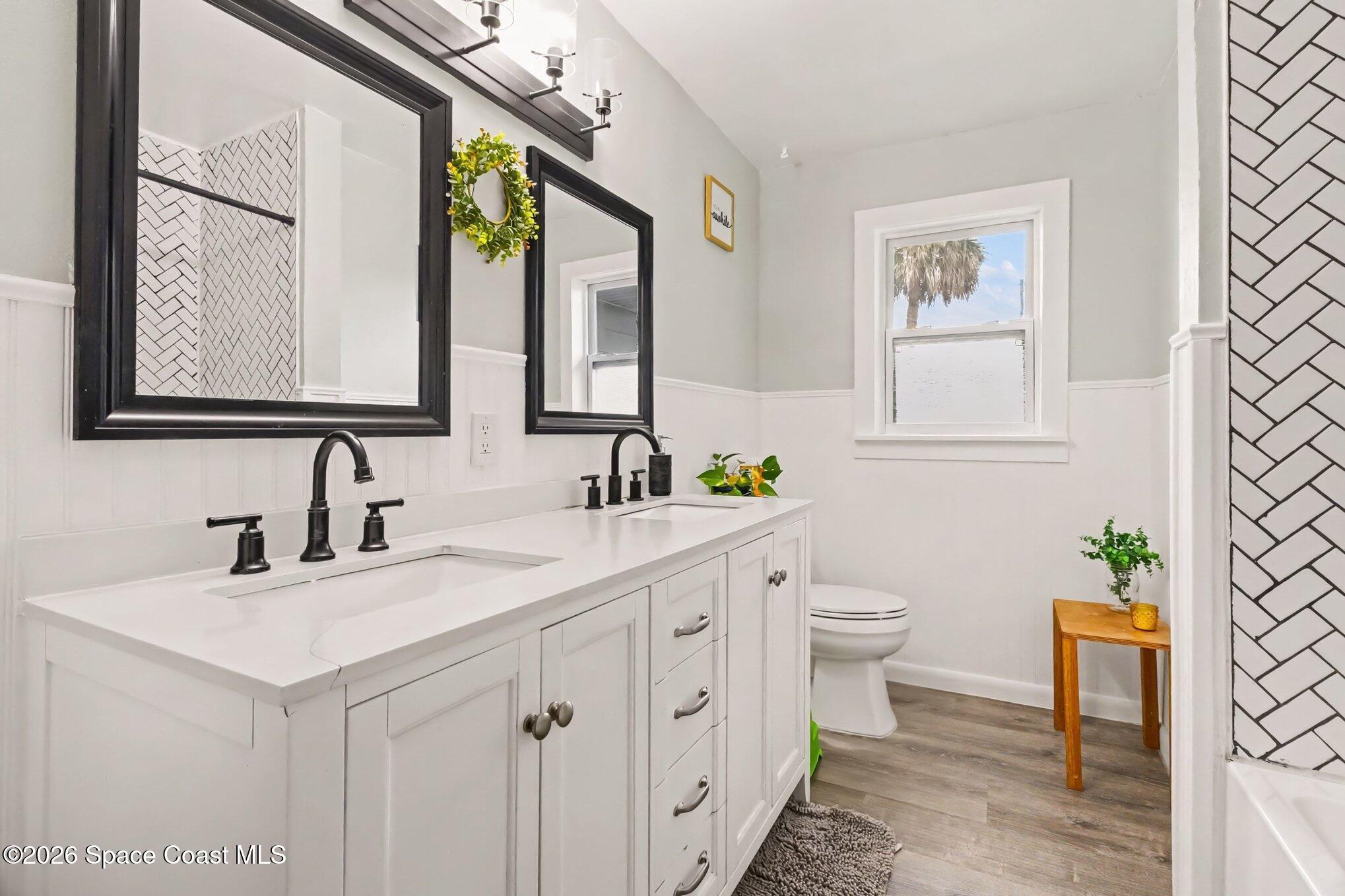 Bright bathroom with a white double vanity, black fixtures, framed mirrors, and herringbone tile accents.