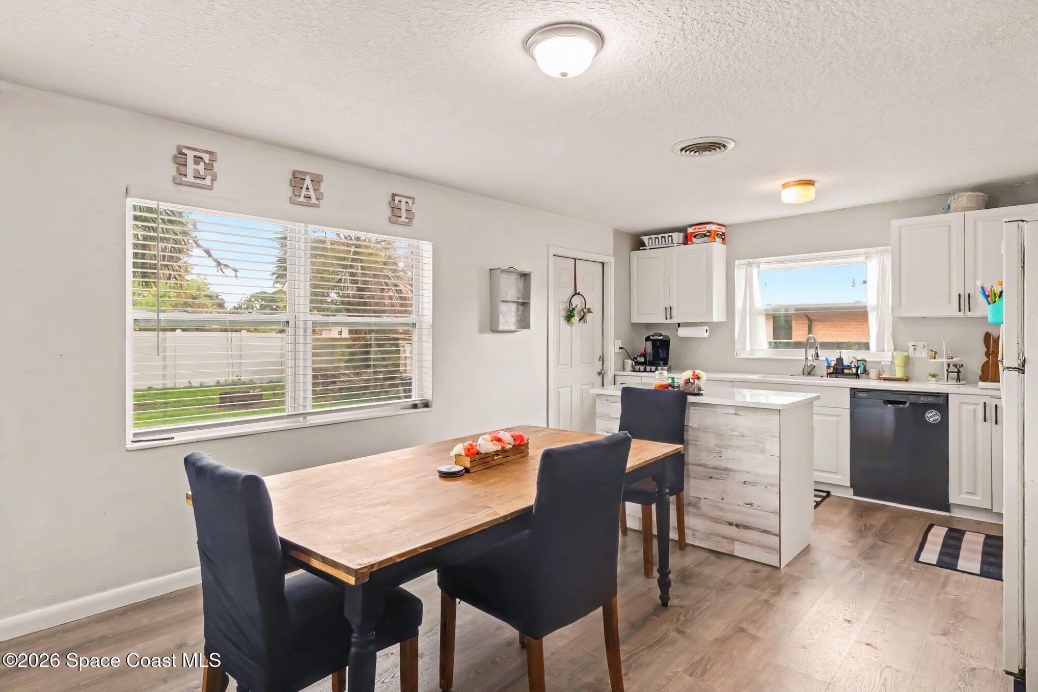 Kitchen and dining area with a wooden table, dark chairs, white cabinets, and large windows.