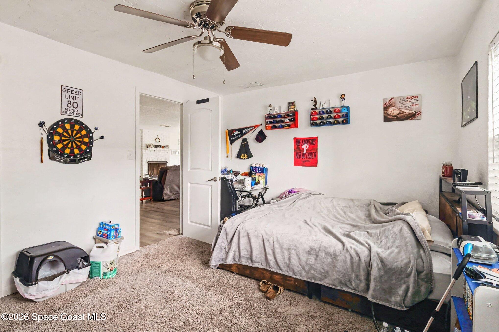 Bedroom with a gray-covered bed, ceiling fan, dartboard, and sports memorabilia.