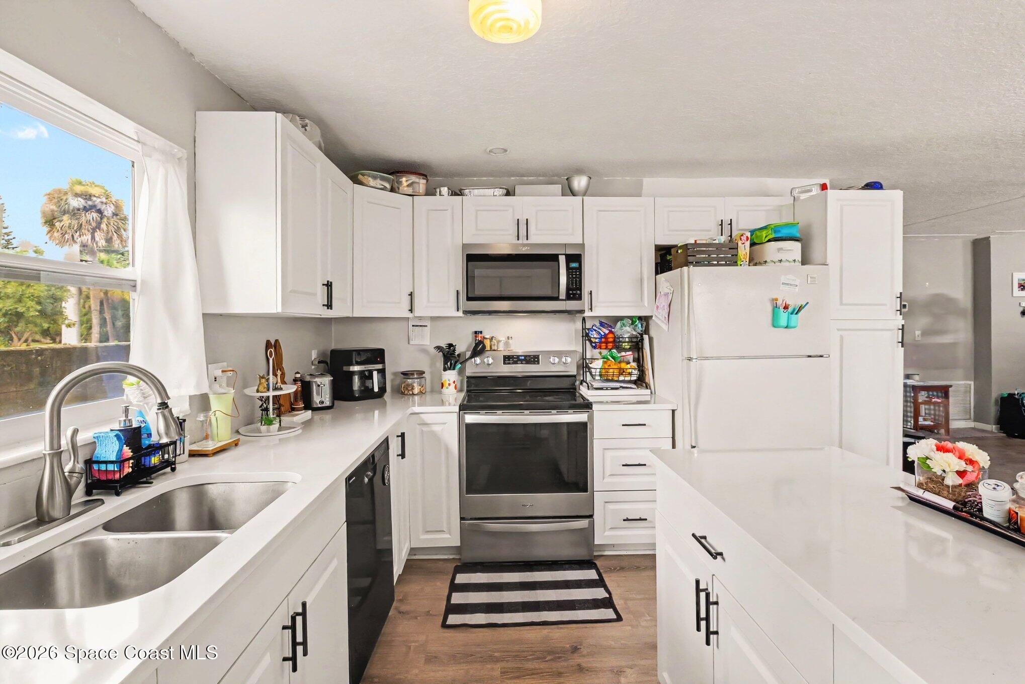 Bright white kitchen with stainless steel appliances, a double-basin sink, and a foreground island.