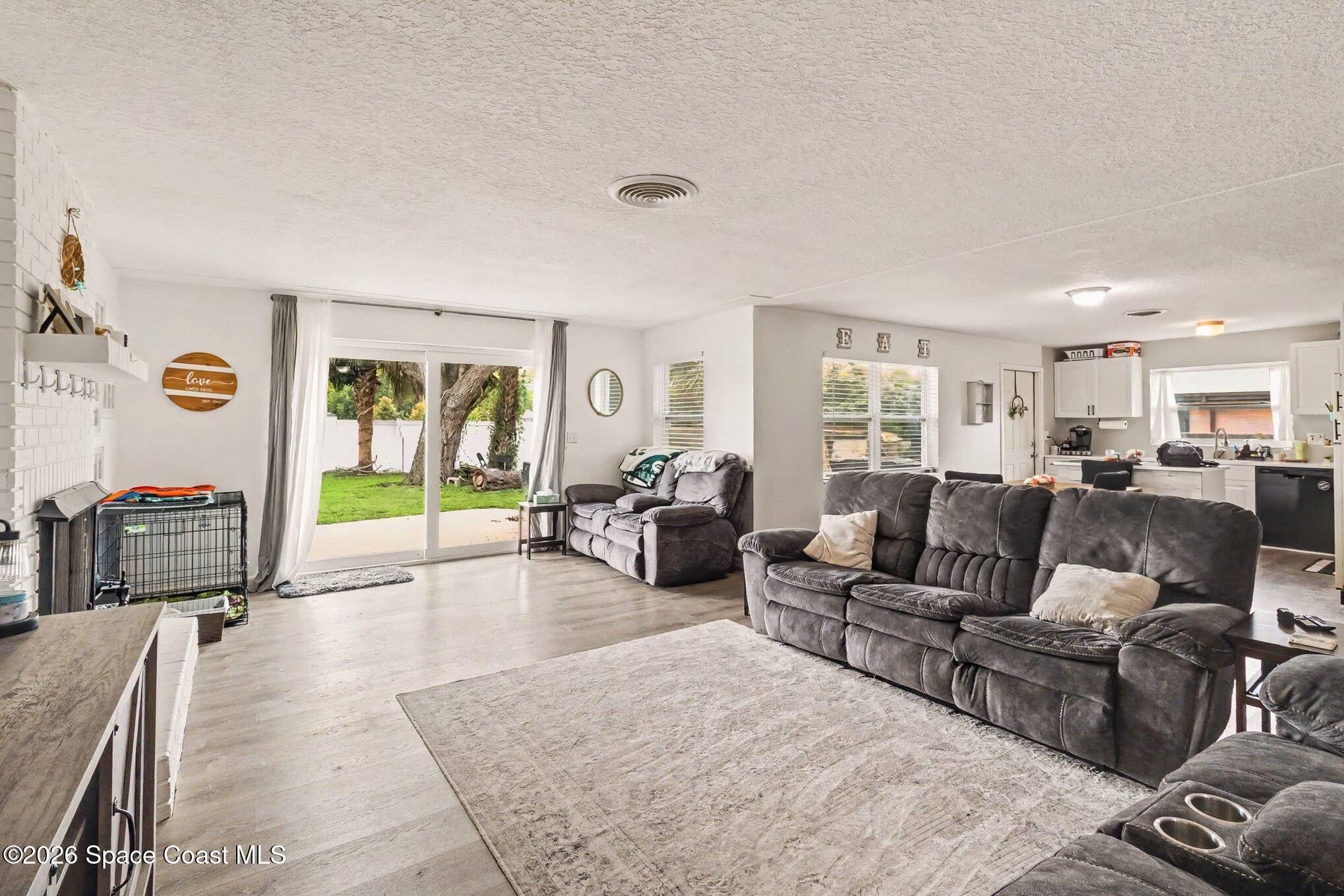 Open-plan living room with gray reclining sofas, a large rug, and sliding doors to the backyard.