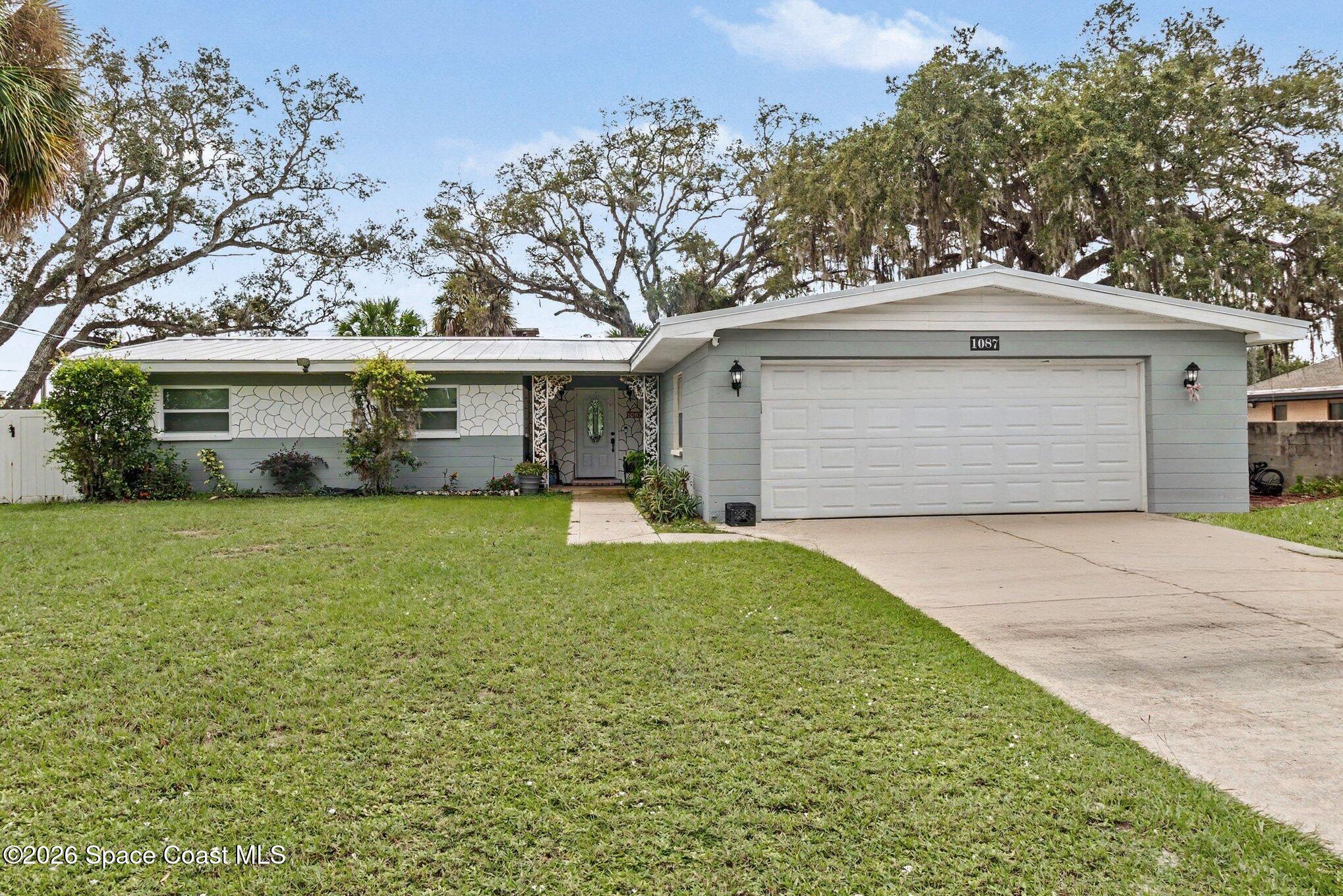 Single-story gray home with an attached garage, broad lawn, and mature oak trees.