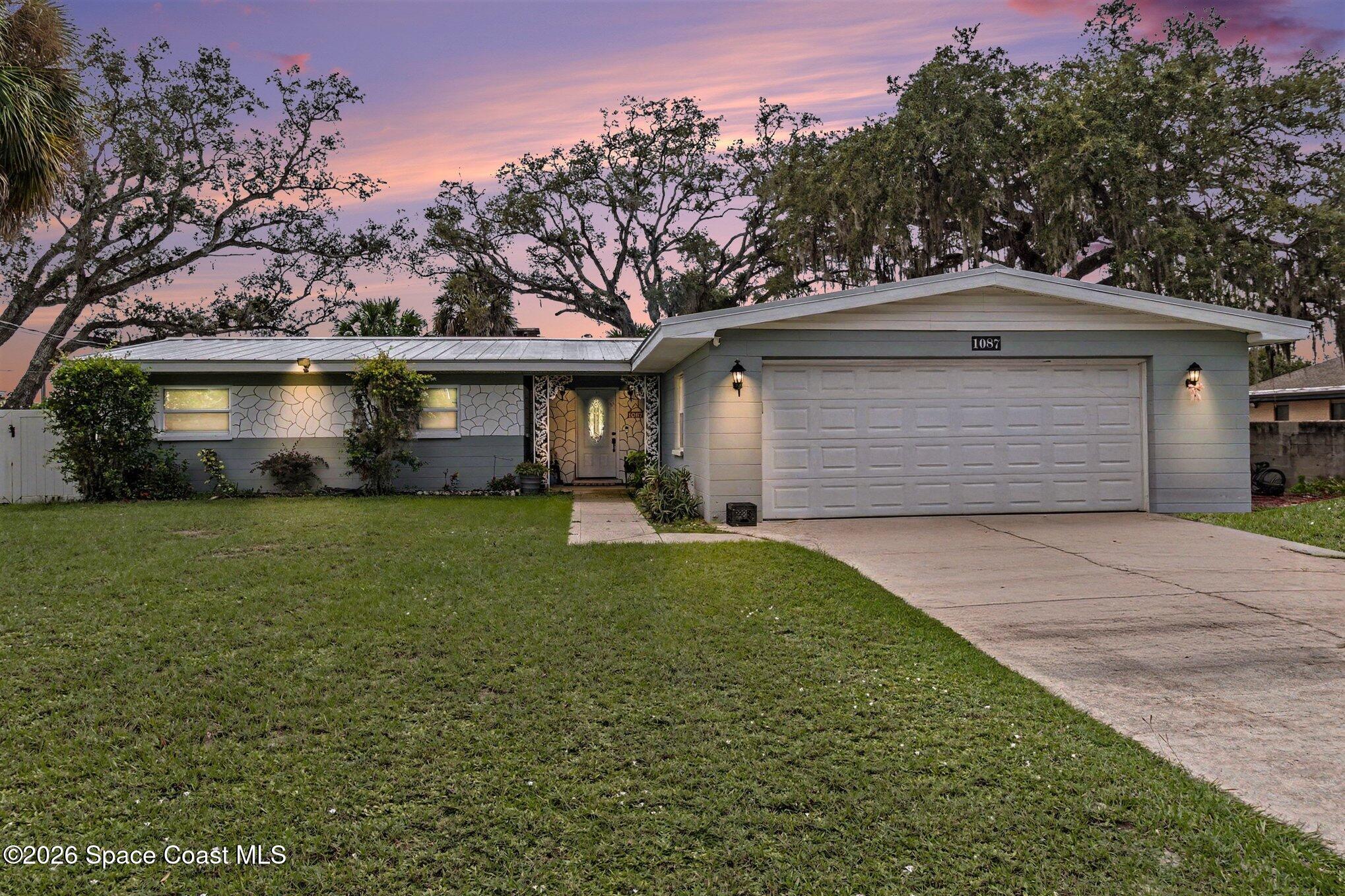 Single-story gray home with a two-car garage and broad lawn beneath a pink dusk sky.