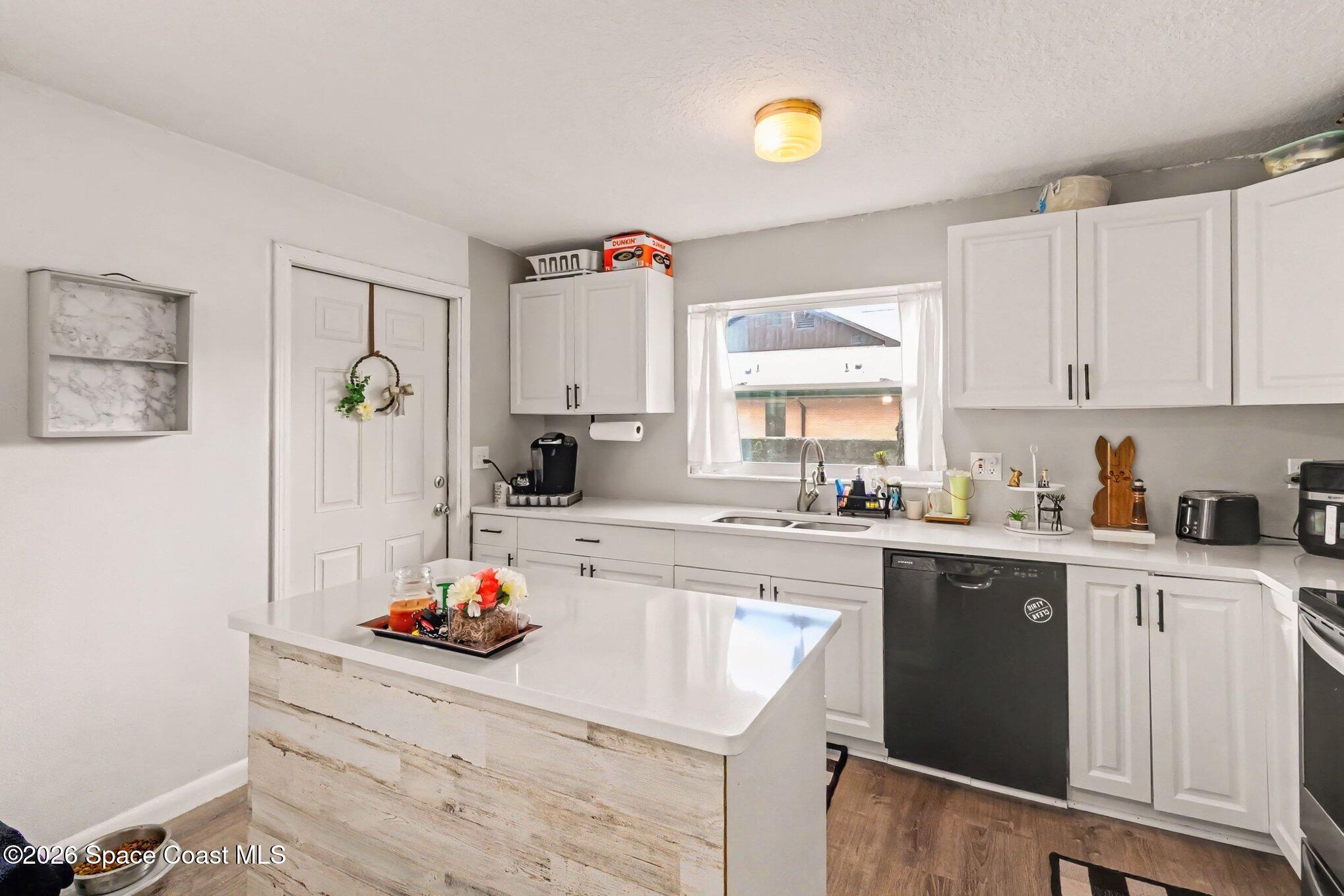 Kitchen with white cabinets, a large island, and a sink beneath a window.