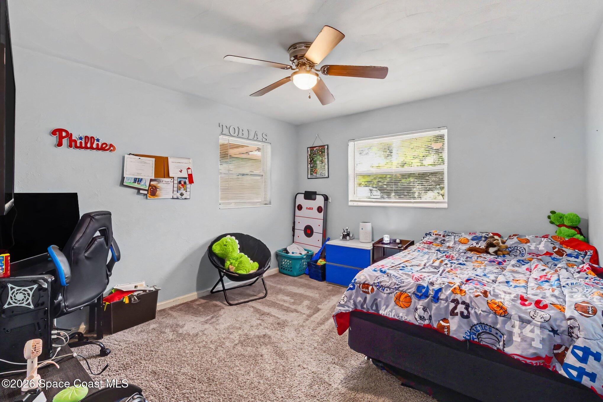 Bedroom with sports-themed bedding, a ceiling fan, and a gaming setup.