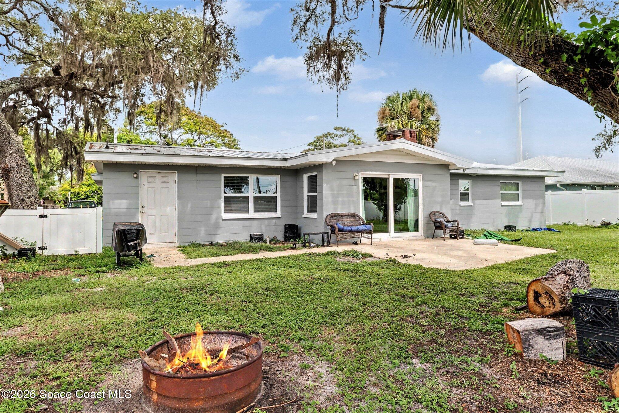 Gray single-story home with a backyard patio, sliding doors, and a fire pit.